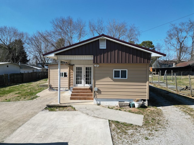 rear view of house featuring entry steps, concrete driveway, fence, french doors, and board and batten siding