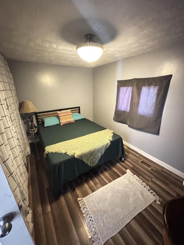 bedroom with visible vents, a textured ceiling, baseboards, and wood finished floors