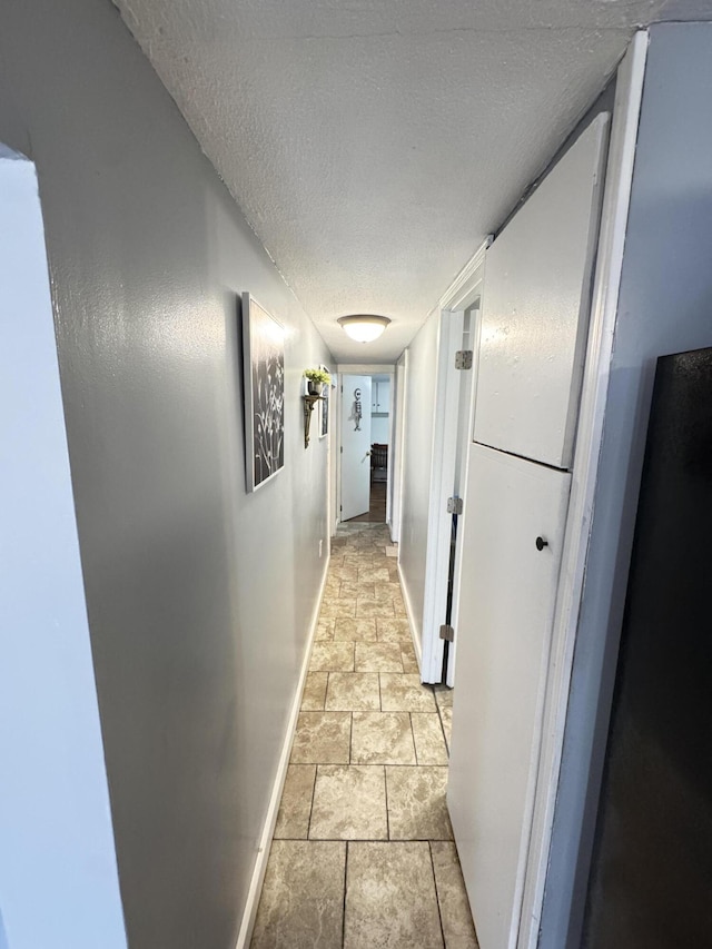 hall with a textured ceiling and baseboards