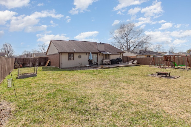 rear view of property featuring a playground, a yard, and a fenced backyard