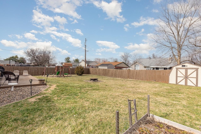 view of yard featuring an outbuilding, a playground, a fenced backyard, a storage shed, and a fire pit