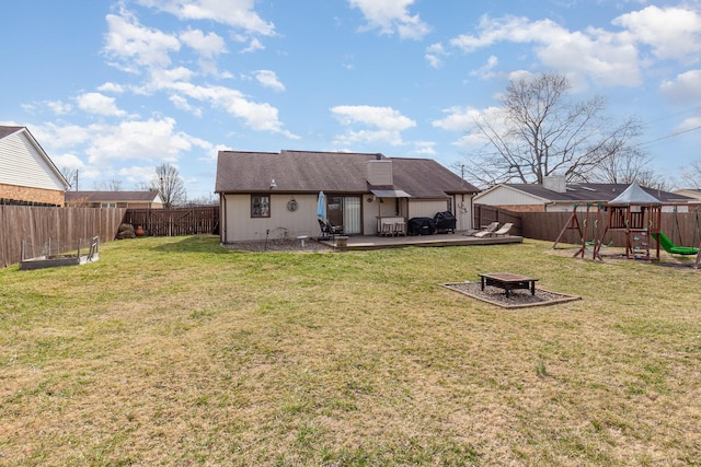 back of property featuring a playground, a yard, a fenced backyard, a fire pit, and a wooden deck