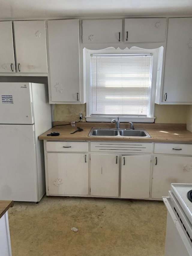 kitchen featuring a sink, white appliances, light floors, and white cabinetry