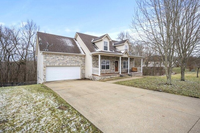 new england style home with a porch, an attached garage, a front yard, stone siding, and driveway