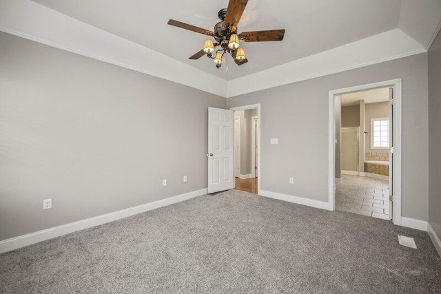 unfurnished bedroom featuring ensuite bath, carpet flooring, a ceiling fan, baseboards, and a raised ceiling