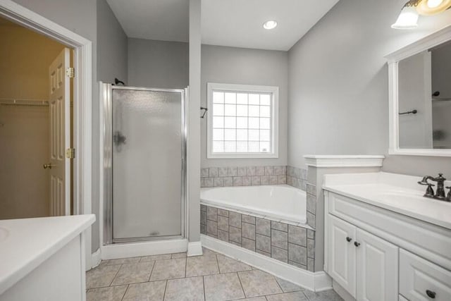 full bathroom featuring a walk in closet, a garden tub, a shower stall, vanity, and tile patterned floors