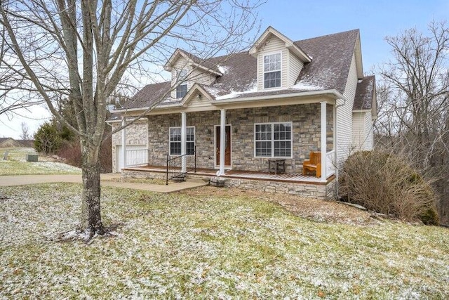 cape cod-style house featuring a porch, stone siding, a front lawn, and a garage