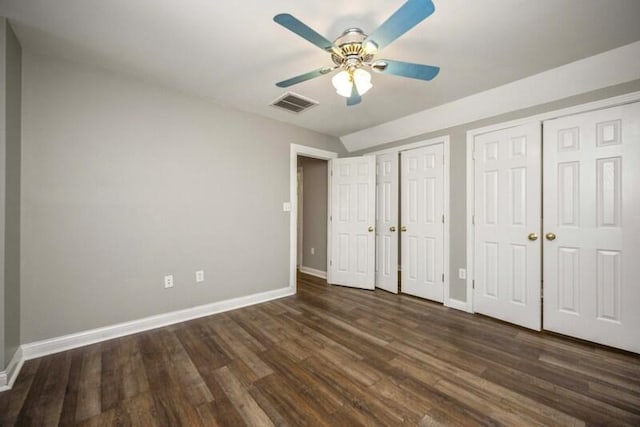 unfurnished bedroom featuring baseboards, visible vents, dark wood finished floors, ceiling fan, and two closets