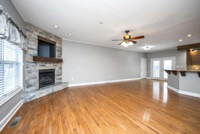 unfurnished living room with a stone fireplace, wood finished floors, visible vents, and baseboards