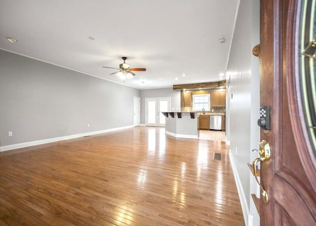 unfurnished living room featuring a ceiling fan, light wood-type flooring, a sink, and baseboards