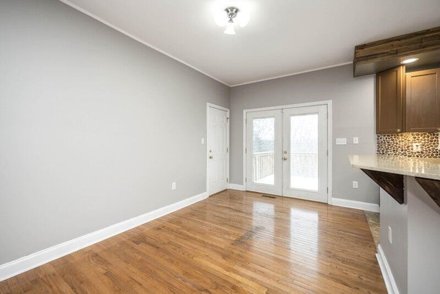 unfurnished dining area featuring light wood-type flooring, baseboards, crown molding, and french doors