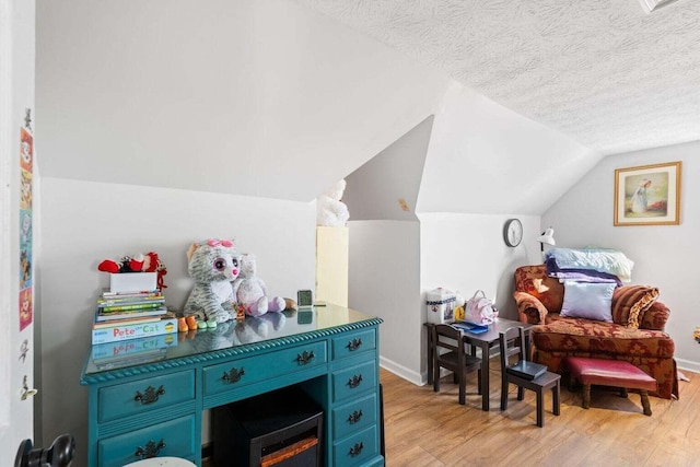 game room featuring a textured ceiling, light wood-type flooring, lofted ceiling, and baseboards