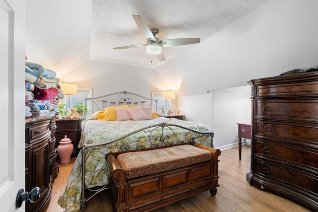 bedroom with lofted ceiling, light wood-style flooring, a ceiling fan, and a textured ceiling