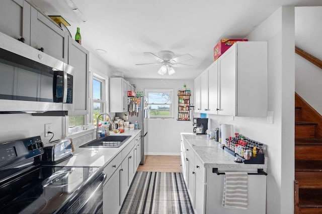 kitchen with a ceiling fan, electric stove, stainless steel microwave, light countertops, and a sink