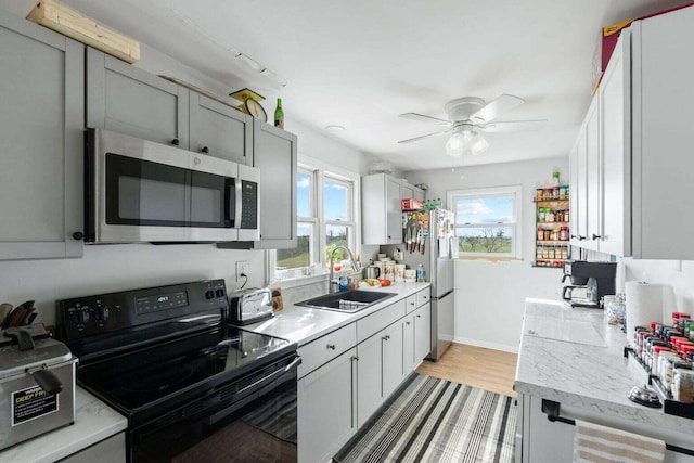 kitchen with stainless steel appliances, a sink, a ceiling fan, light wood-style floors, and light countertops