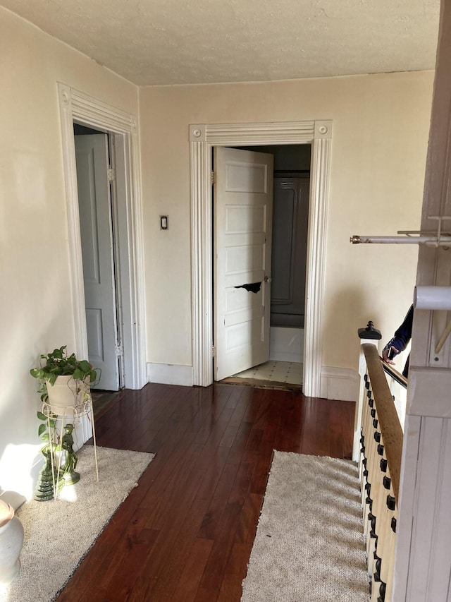 corridor with a textured ceiling, baseboards, and dark wood-style flooring