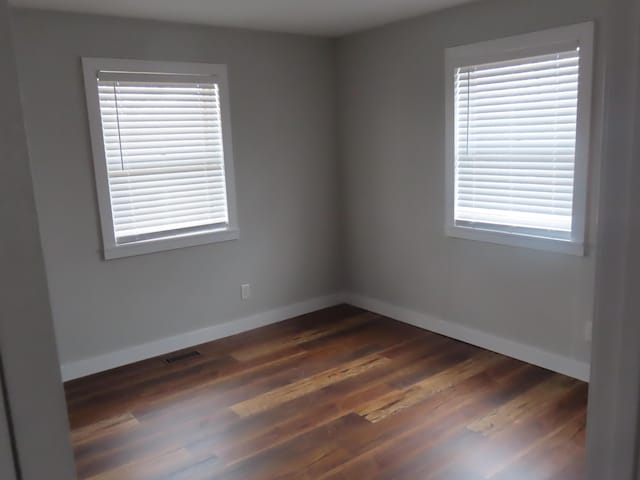 spare room featuring dark wood-style floors, visible vents, and baseboards