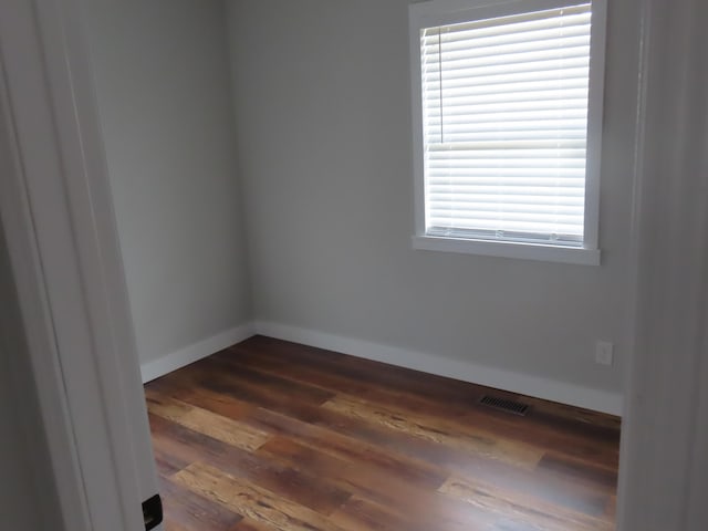 unfurnished room featuring dark wood-style flooring, visible vents, and baseboards