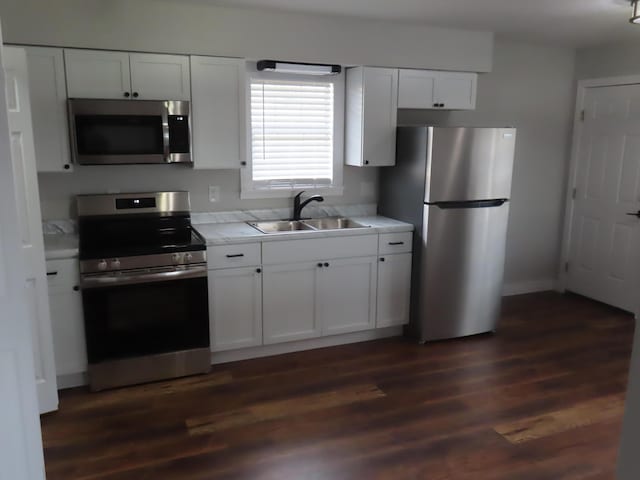 kitchen with white cabinets, dark wood finished floors, appliances with stainless steel finishes, light countertops, and a sink