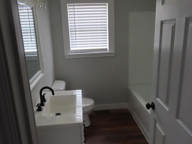 full bathroom with baseboards, toilet, wood finished floors, vanity, and a bath