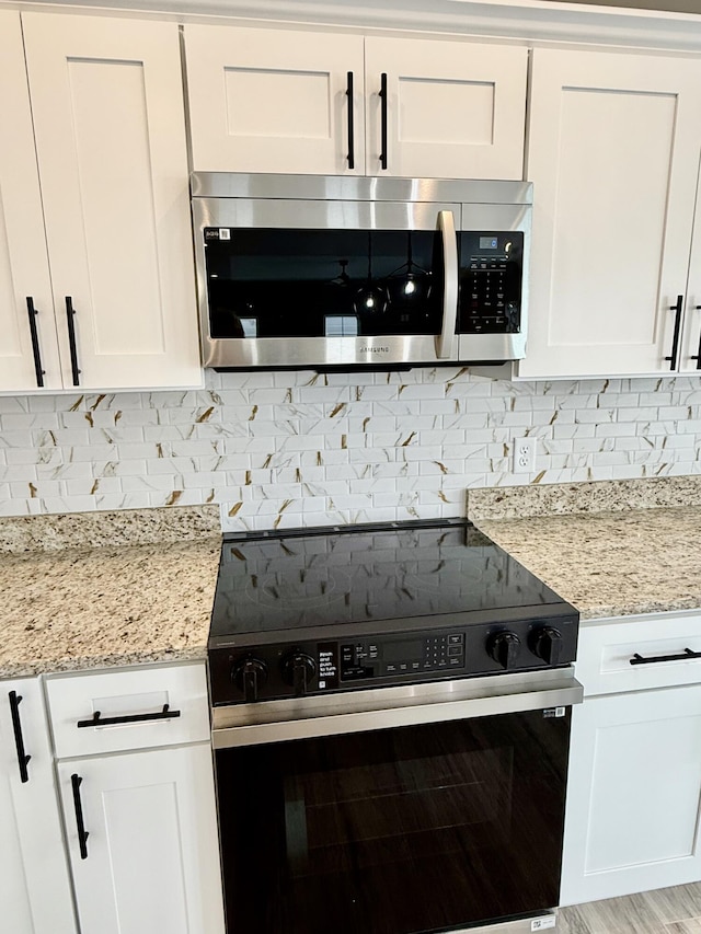 kitchen with electric stove, stainless steel microwave, white cabinetry, decorative backsplash, and light stone countertops