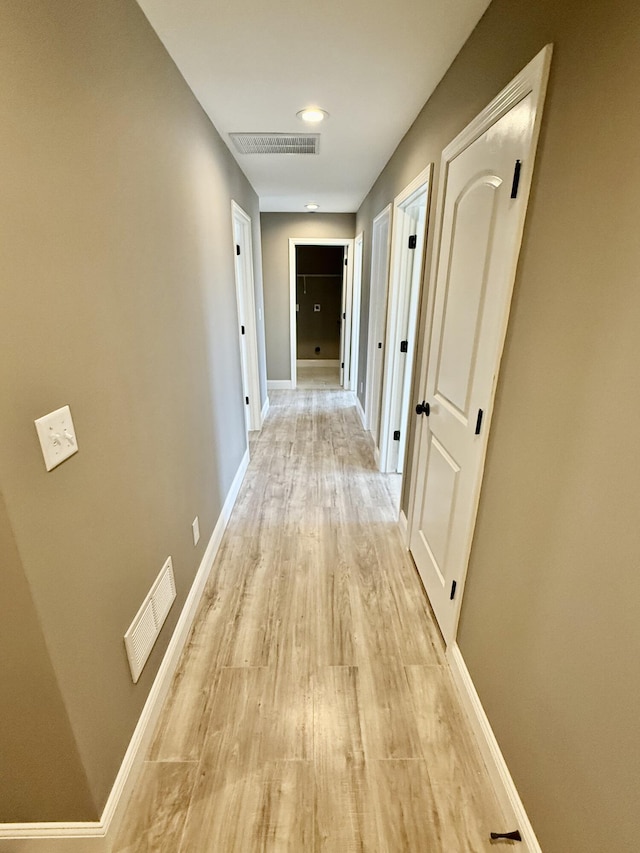 hallway with visible vents, baseboards, and light wood finished floors