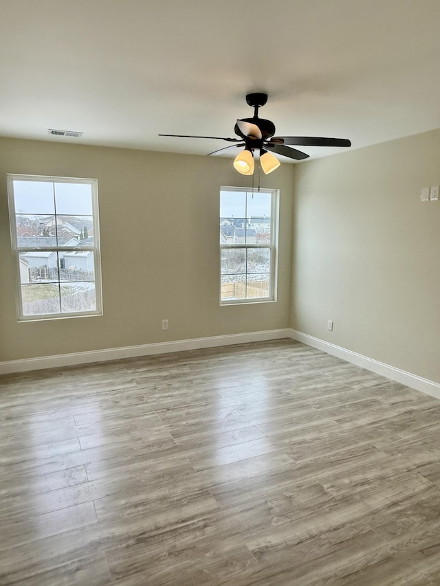 empty room featuring visible vents, plenty of natural light, baseboards, and wood finished floors