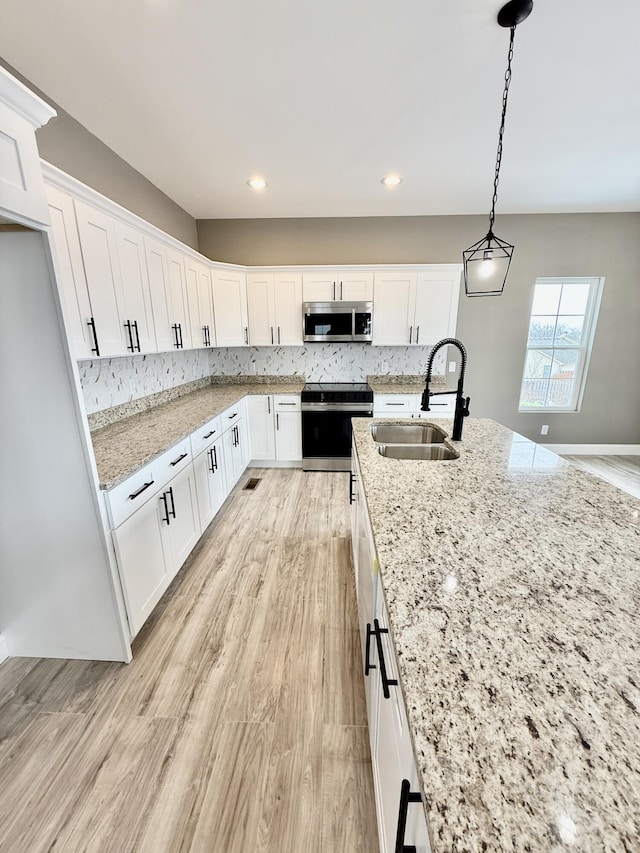 kitchen featuring range with electric cooktop, a sink, stainless steel microwave, tasteful backsplash, and white cabinets