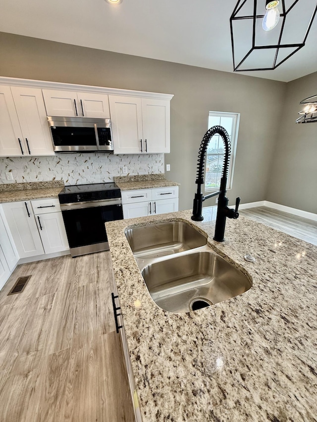 kitchen with electric range, visible vents, a sink, stainless steel microwave, and white cabinetry