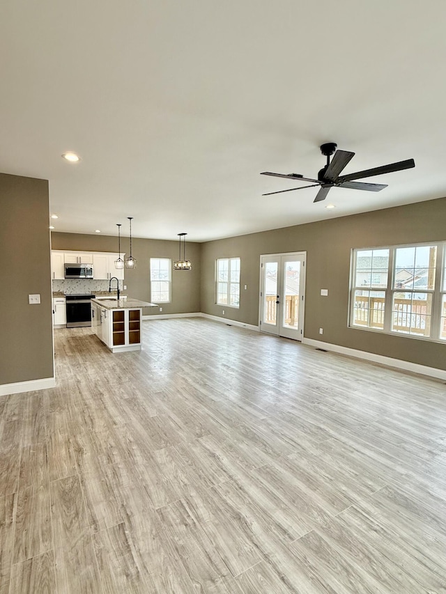 unfurnished living room with ceiling fan, light wood-style floors, baseboards, and a sink