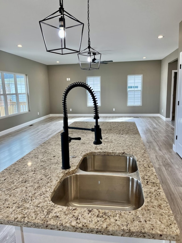 interior details with light stone countertops, decorative light fixtures, recessed lighting, wood finished floors, and a sink