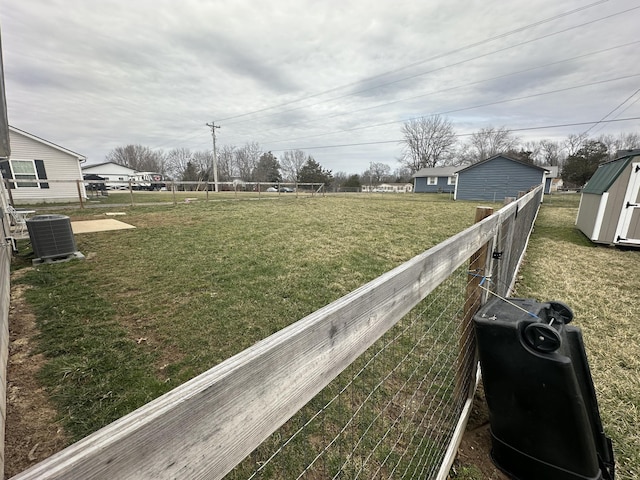 view of yard with a storage unit, fence, central AC, and an outbuilding