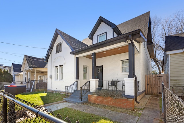 view of front of home featuring a shingled roof, covered porch, a gate, fence, and brick siding