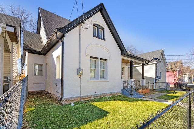 rear view of property featuring a fenced backyard, a yard, brick siding, and roof with shingles