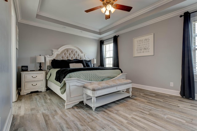 bedroom with baseboards, a raised ceiling, light wood-style floors, and ornamental molding