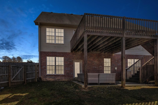 back of house at dusk featuring a patio, fence, a yard, brick siding, and stairs