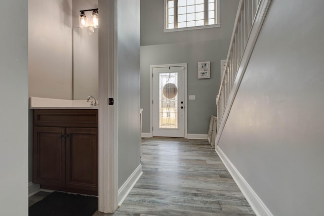 foyer entrance featuring stairs, light wood-style flooring, baseboards, and a towering ceiling