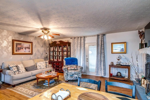 living room with ceiling fan, a textured ceiling, a fireplace, and wood finished floors