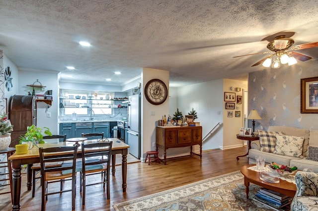 living area featuring ceiling fan, a textured ceiling, baseboards, and wood finished floors