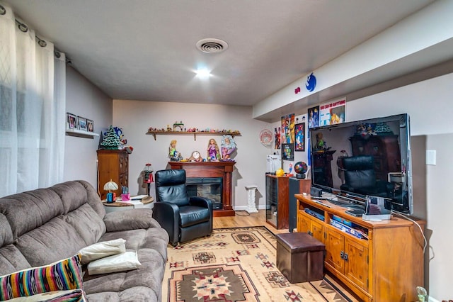 living area with light wood-style flooring, visible vents, and a glass covered fireplace