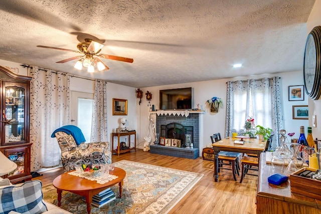 living room with light wood-type flooring, ceiling fan, a fireplace, and a wealth of natural light