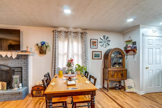 dining area with a brick fireplace, a textured ceiling, baseboards, and wood finished floors