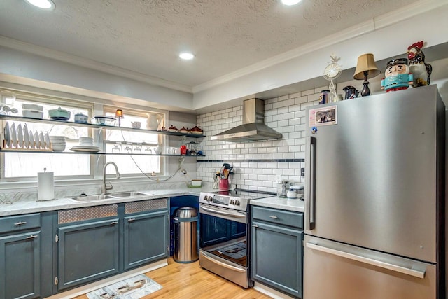 kitchen featuring light wood-style flooring, stainless steel appliances, wall chimney range hood, open shelves, and a sink