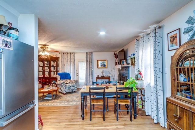 dining area with a fireplace, a ceiling fan, and light wood-style floors