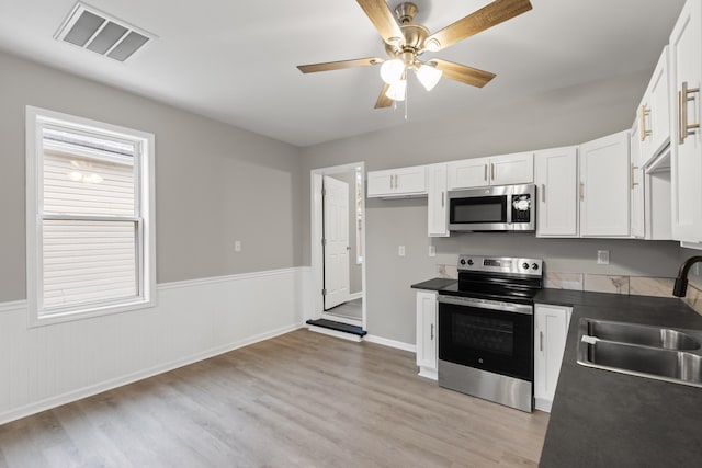 kitchen with visible vents, a sink, stainless steel appliances, white cabinetry, and dark countertops