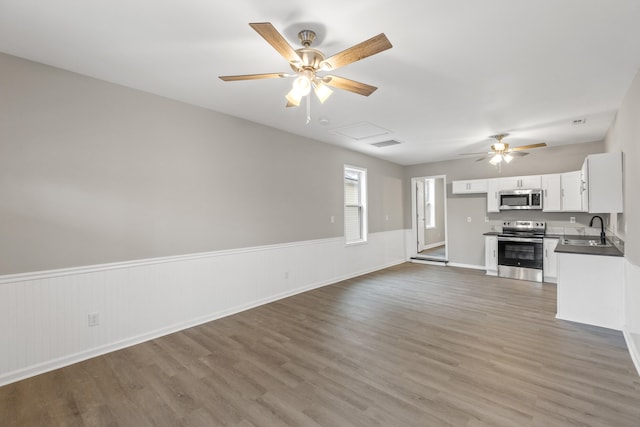 unfurnished living room featuring wainscoting, light wood-style floors, and a sink