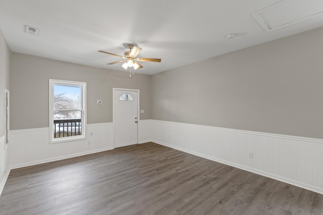 spare room with ceiling fan, visible vents, dark wood-style flooring, and wainscoting