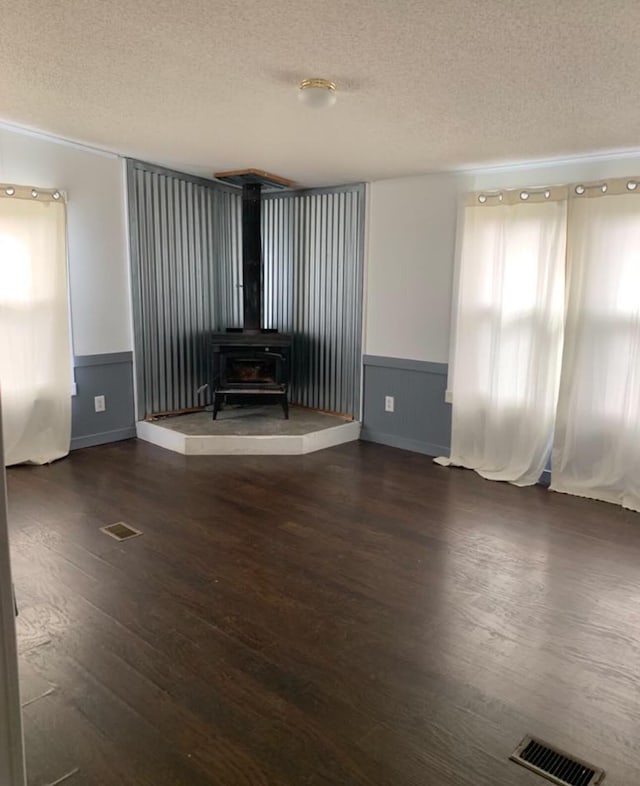 unfurnished living room with a textured ceiling, a wainscoted wall, wood finished floors, visible vents, and a wood stove