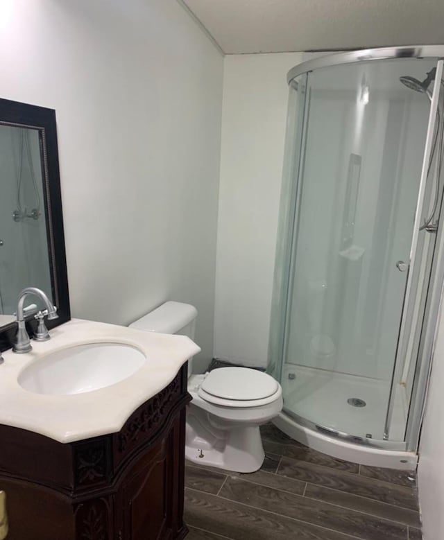 bathroom featuring toilet, a stall shower, vanity, and wood tiled floor