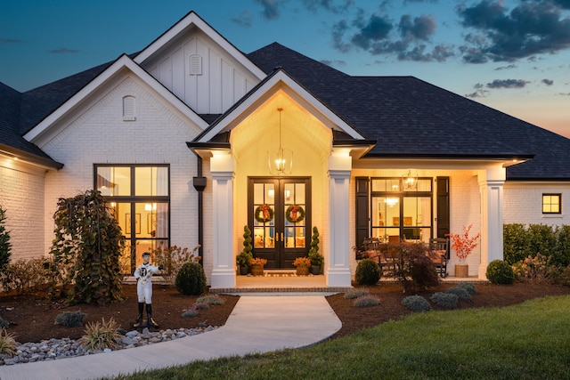 view of front facade featuring french doors, brick siding, roof with shingles, covered porch, and board and batten siding